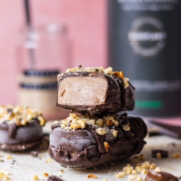 Vegan Chocolate Hazelnut Magnum Ice Cream, one cut open laying on top of another one, protein tub blurry in the background, on pink backdrop