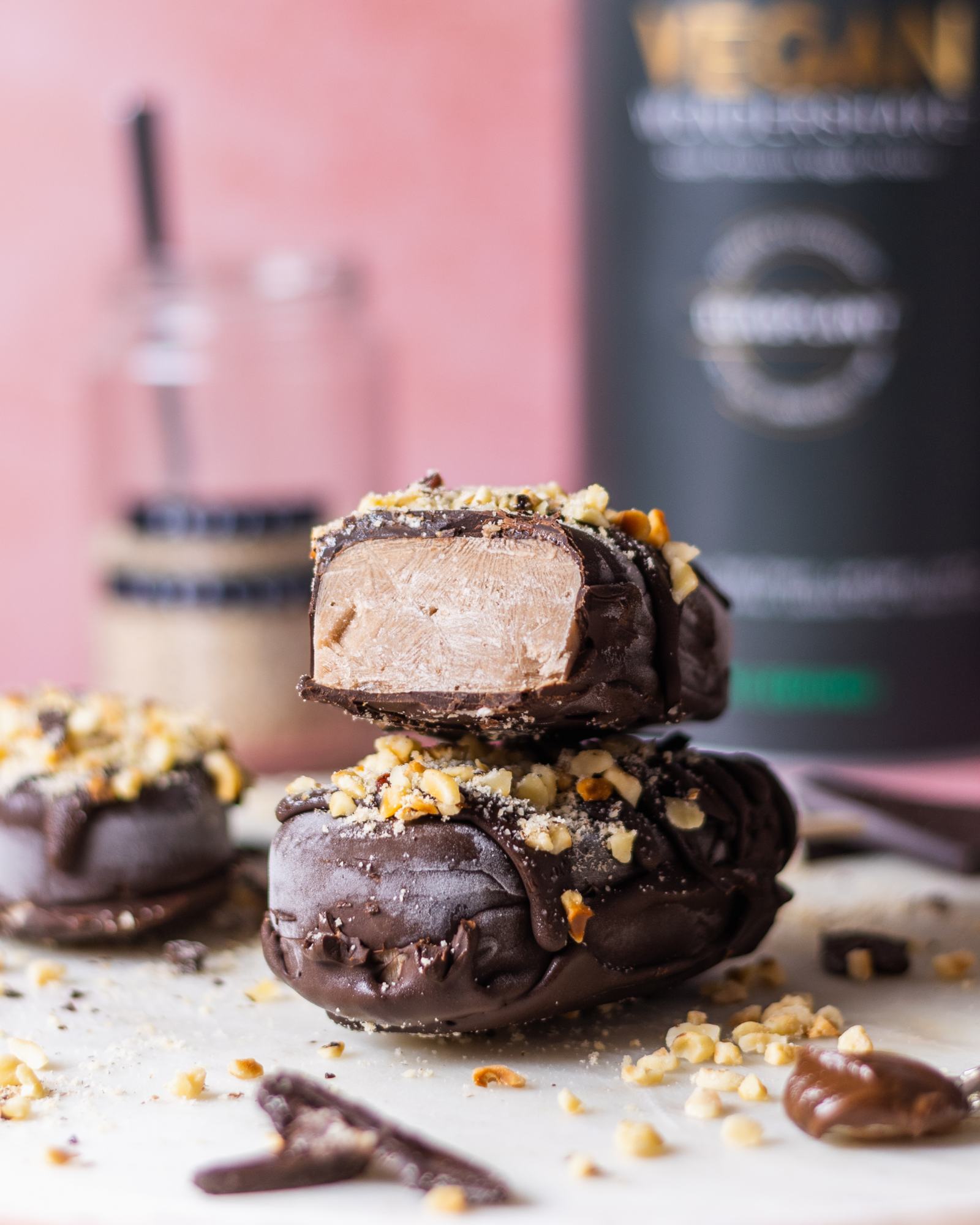 Vegan Chocolate Hazelnut Magnum Ice Cream, one cut open laying on top of another one, protein tub blurry in the background, on pink backdrop