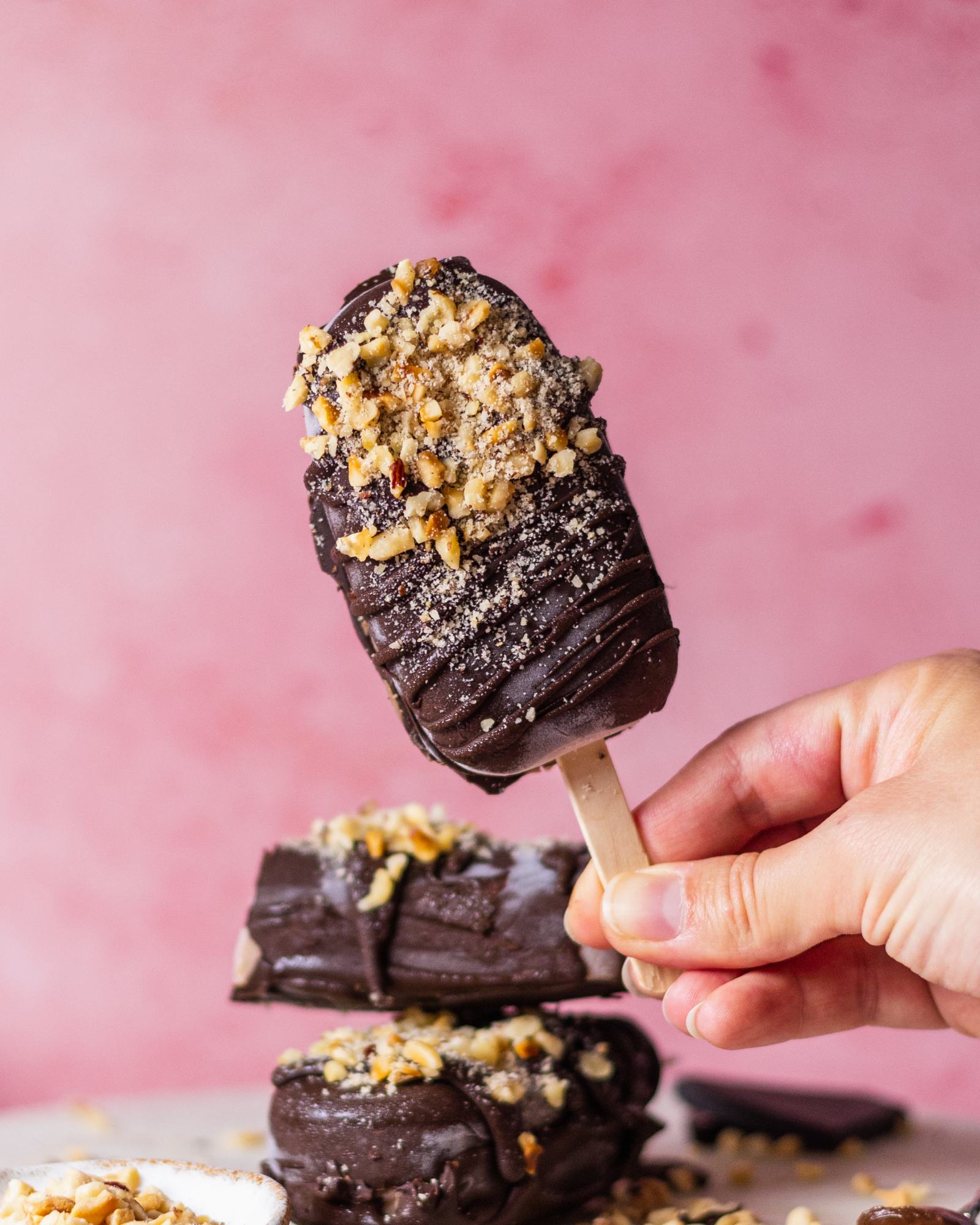 Vegan Chocolate Hazelnut Magnum Ice Cream held in one hand on pink background