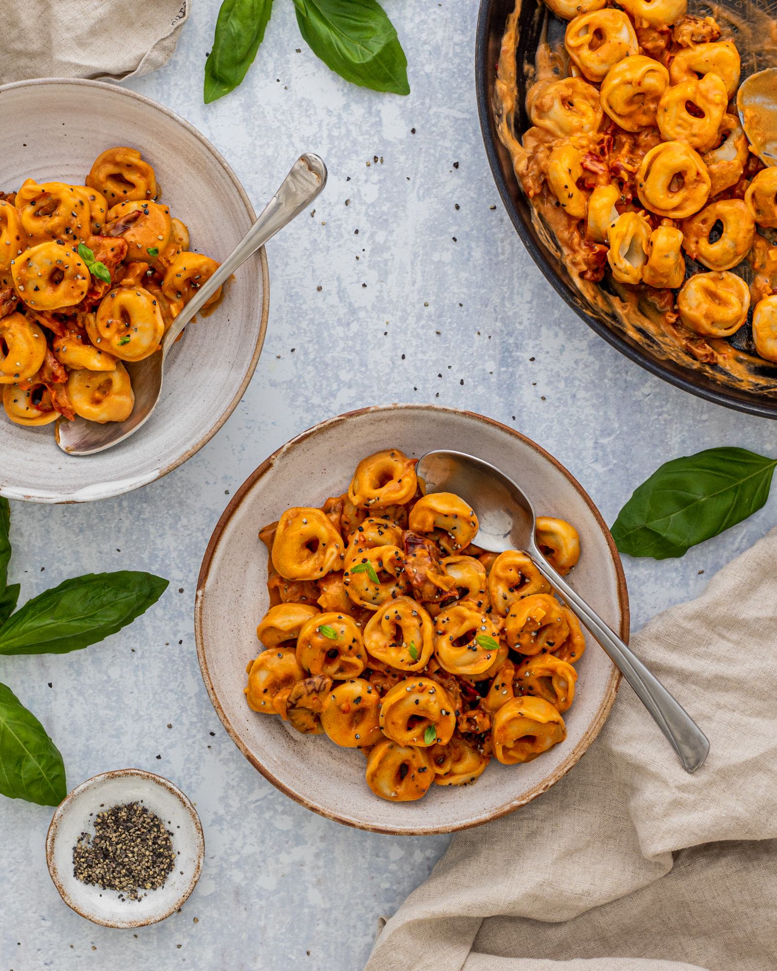 Creamy Sun-Dried Tomato Pasta - Vegan Tortellini served onto 2 plates with the pan standing next to it on a bright table top