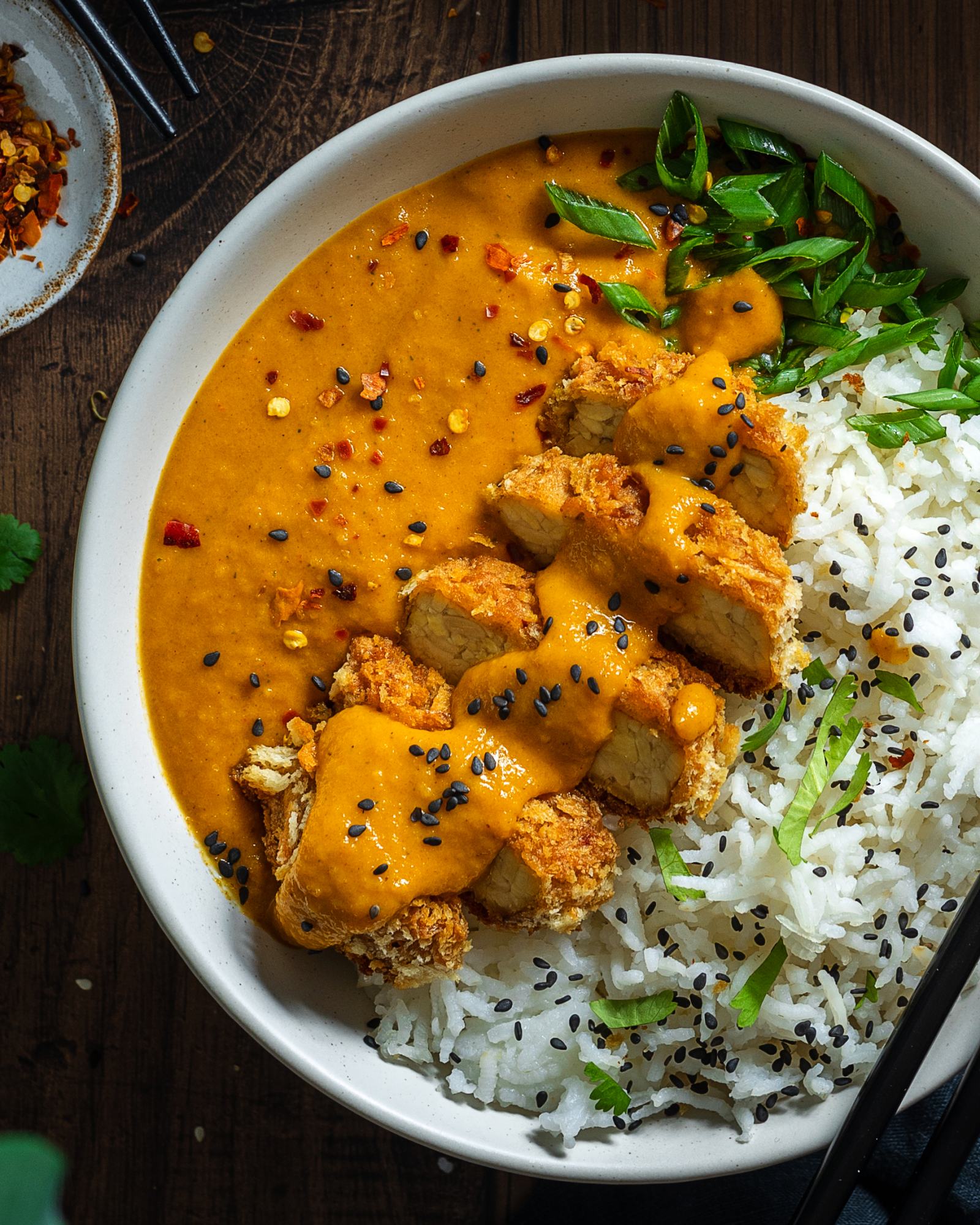 Bowl full of Vegan Katsu Curry with Tempeh, Close Up, rice and katsu sauce in the bowl, sliced crunchy panko coated tempeh on top with a drizzle of tonkatsu style sauce