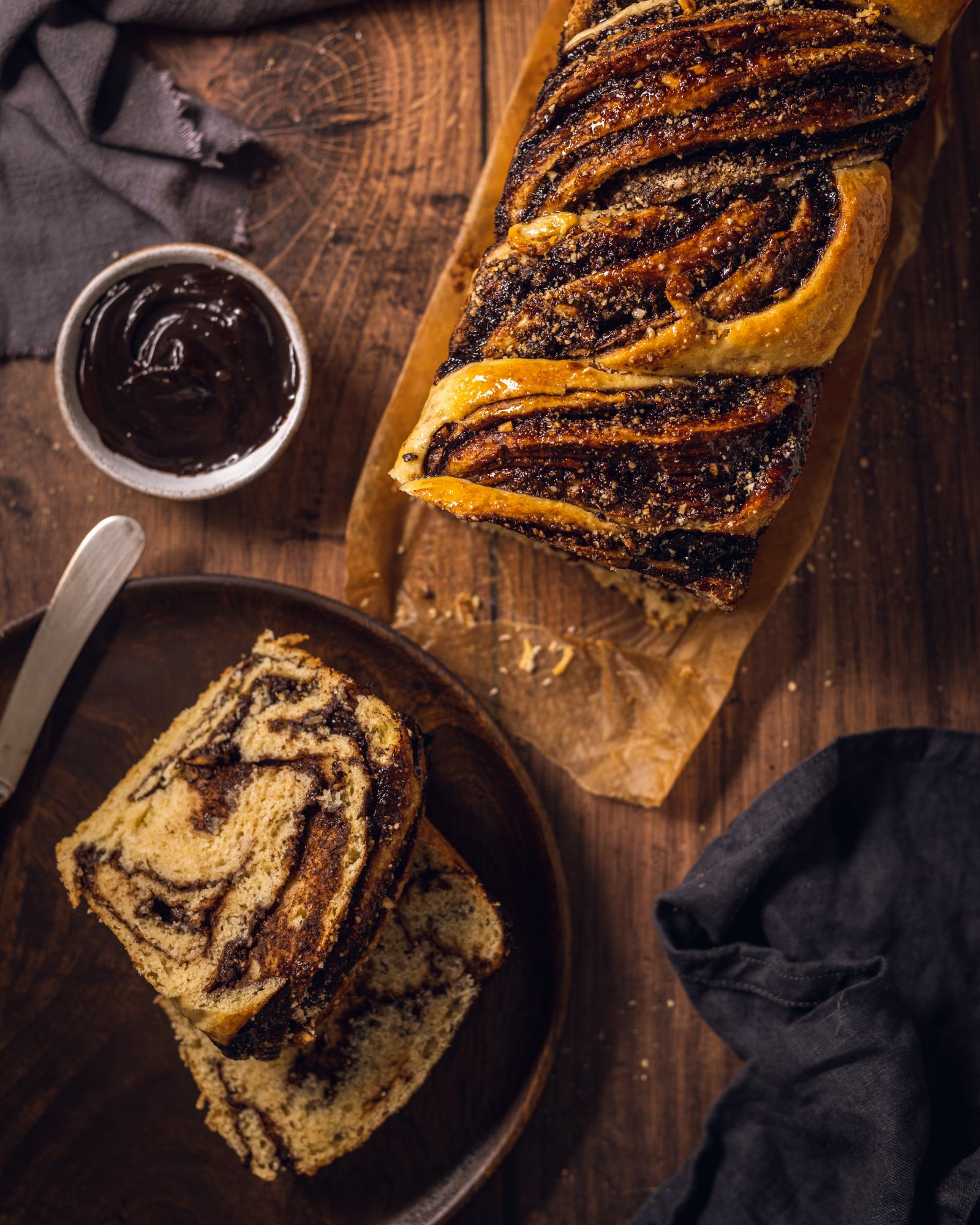 Vegan chocolate babka on a wooden table with two slices on a plate.