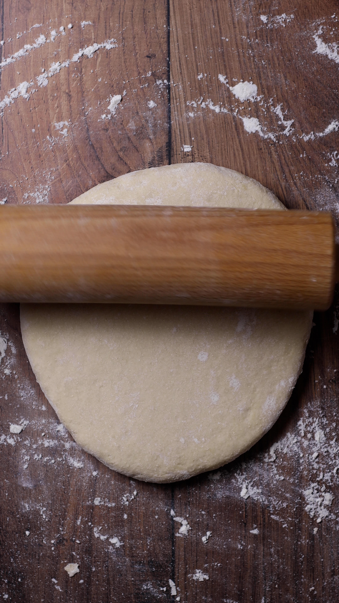 A wooden rolling pin  unolling the dough on a wooden surface