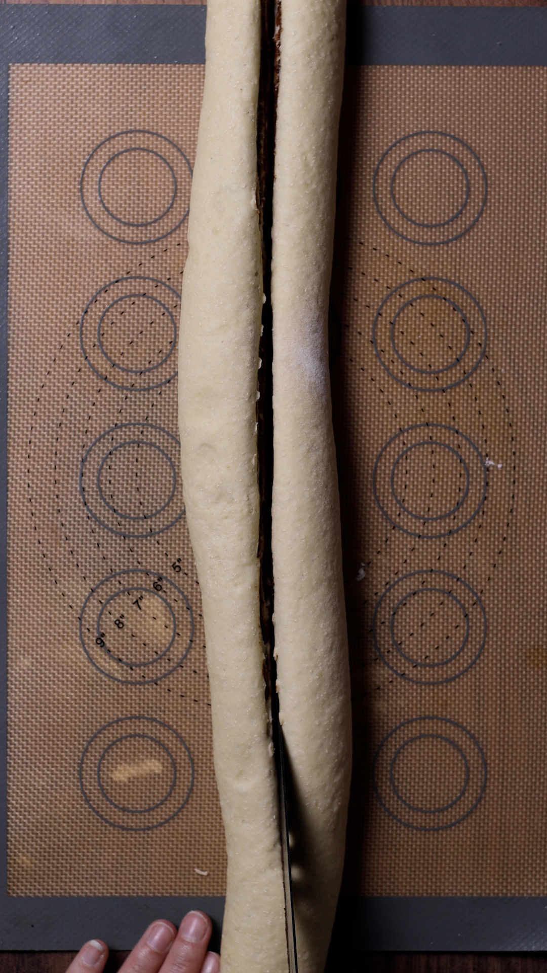 A knife slicing rolled babka dough in half.