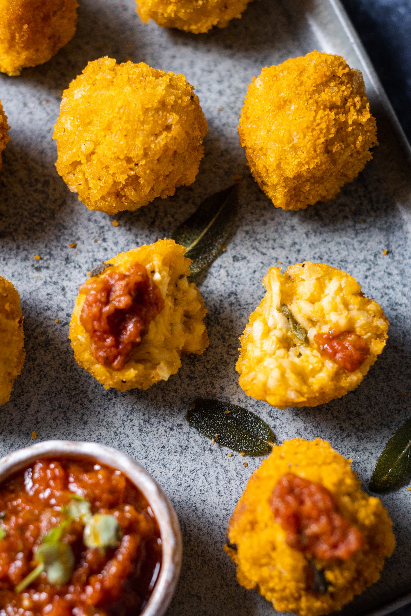 a pumpkin arancini cut in half on a serving platter, shown up close with the pumpkin risotto shown inside the crunchy arancini