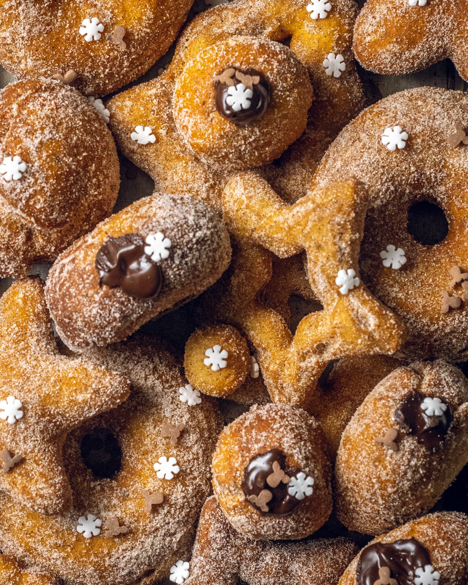 A selection of vegan cinnamon donuts of different shapes and sizes, all of them coated with cinnamon sugar.