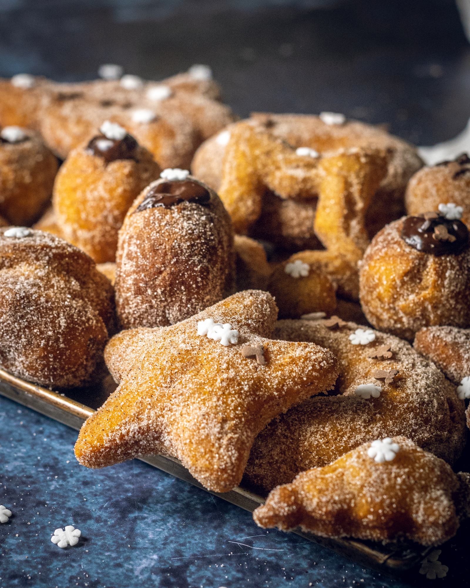 Multiple cinnamon sugar donuts in different shapes on a baking tray with sprinkles on top.