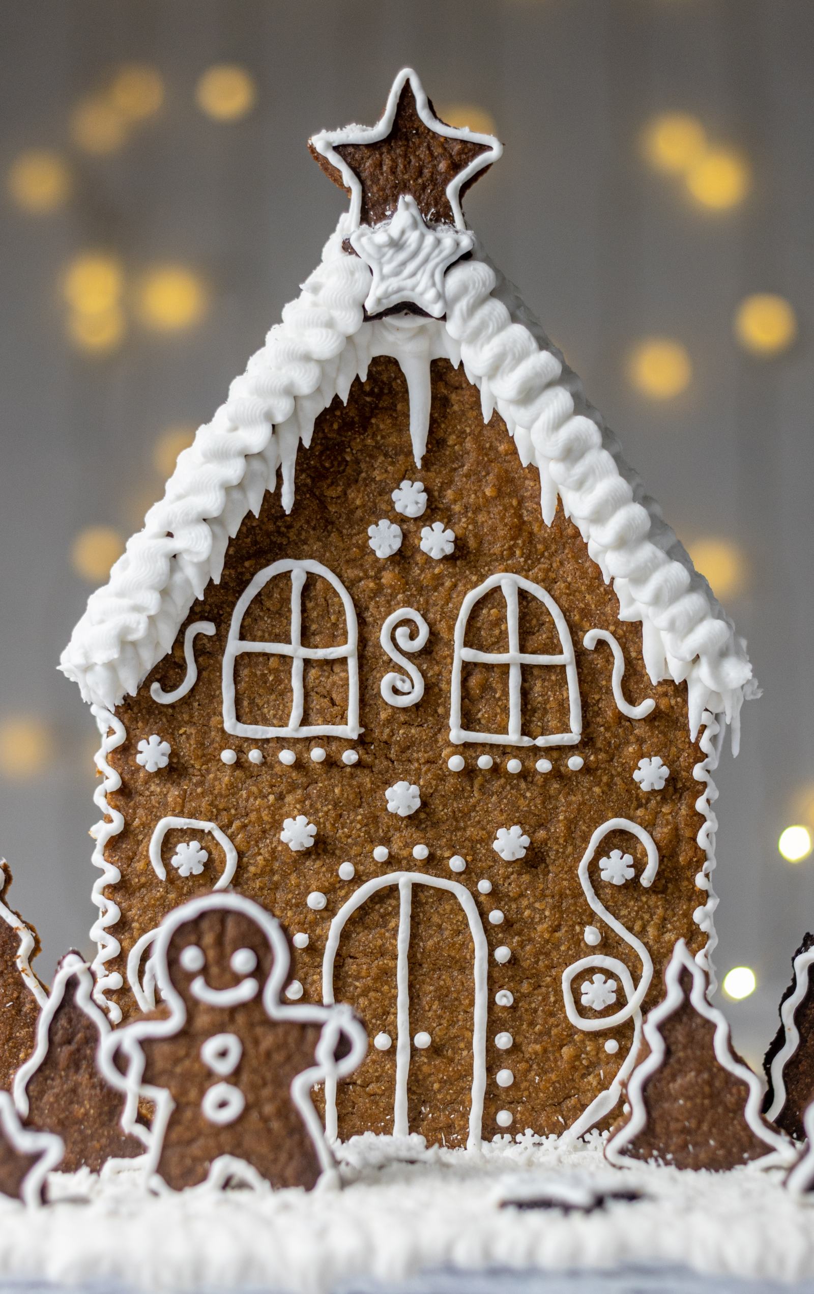 Front view of the homemade house with a door at the bottom and two windows on the first floor, decorate it with white Royal icing made to a vegan recipe.