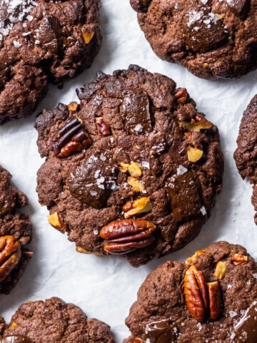 Vegan Triple Chocolate and Pecan Cookies. photographed from above, arranged on white baking parchment