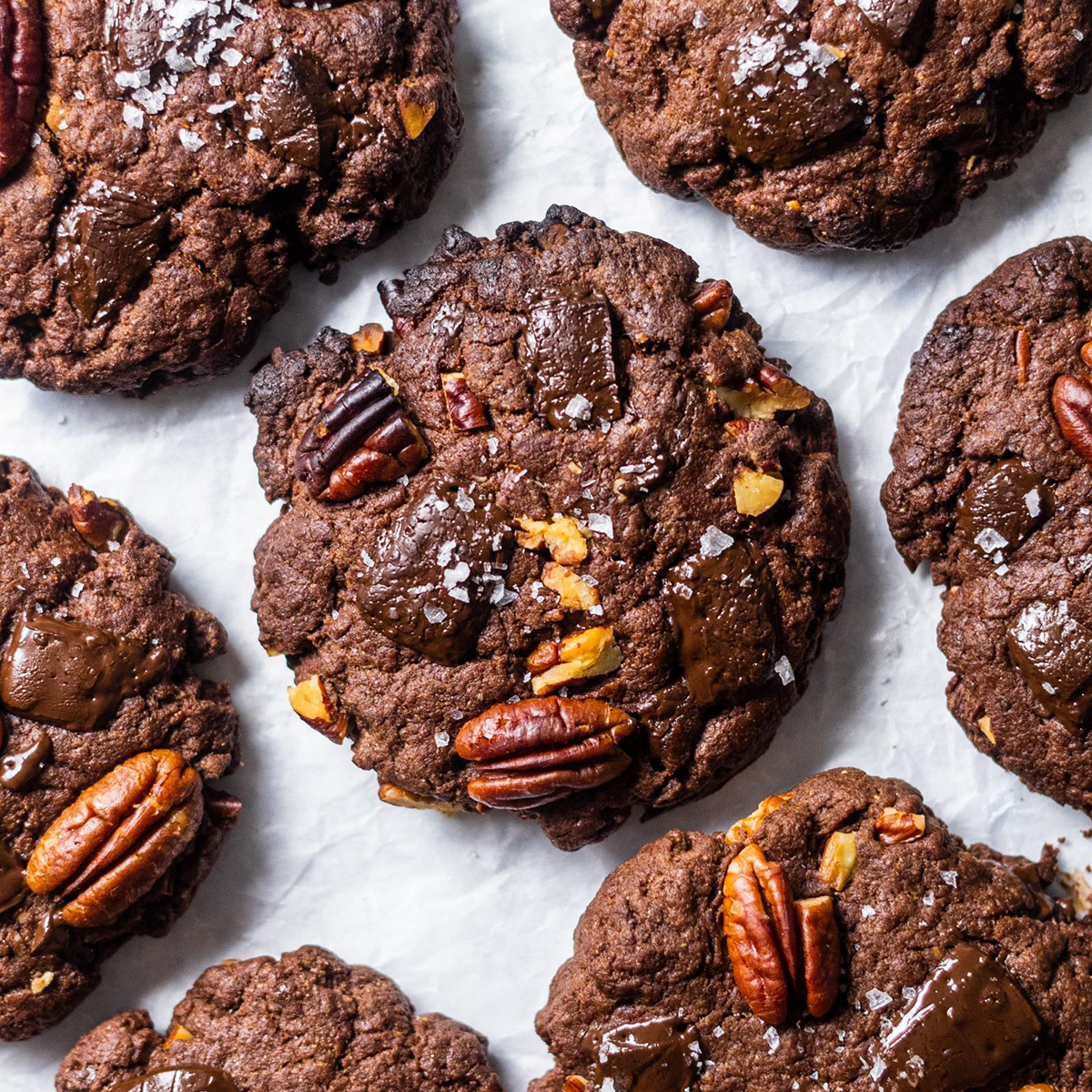 Vegan Triple Chocolate and Pecan Cookies. photographed from above, arranged on white baking parchment