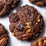 Vegan Triple Chocolate and Pecan Cookies. photographed from above, arranged on white baking parchment