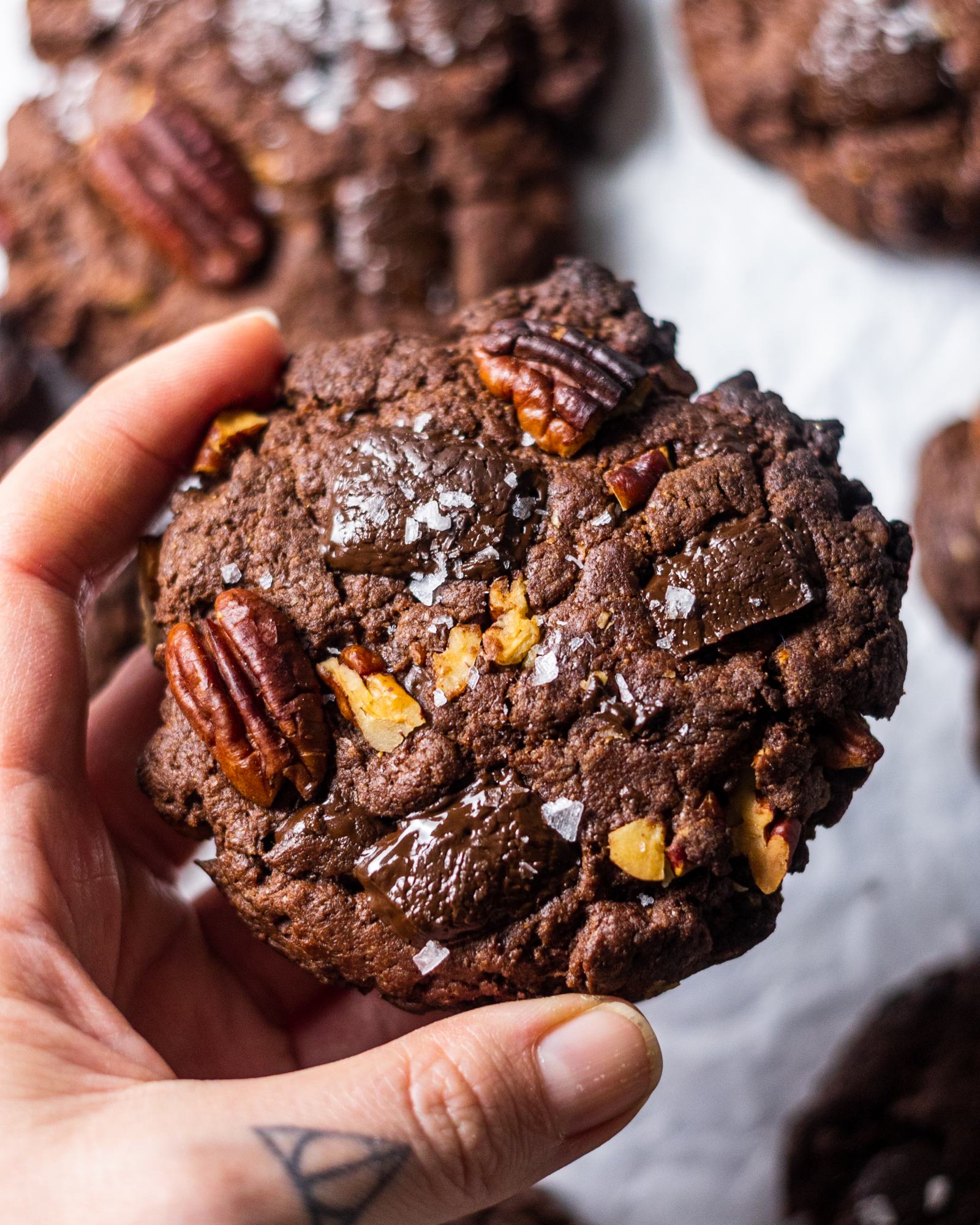 Hand holding a Vegan Triple Chocolate and Pecan Cookie with sea salt