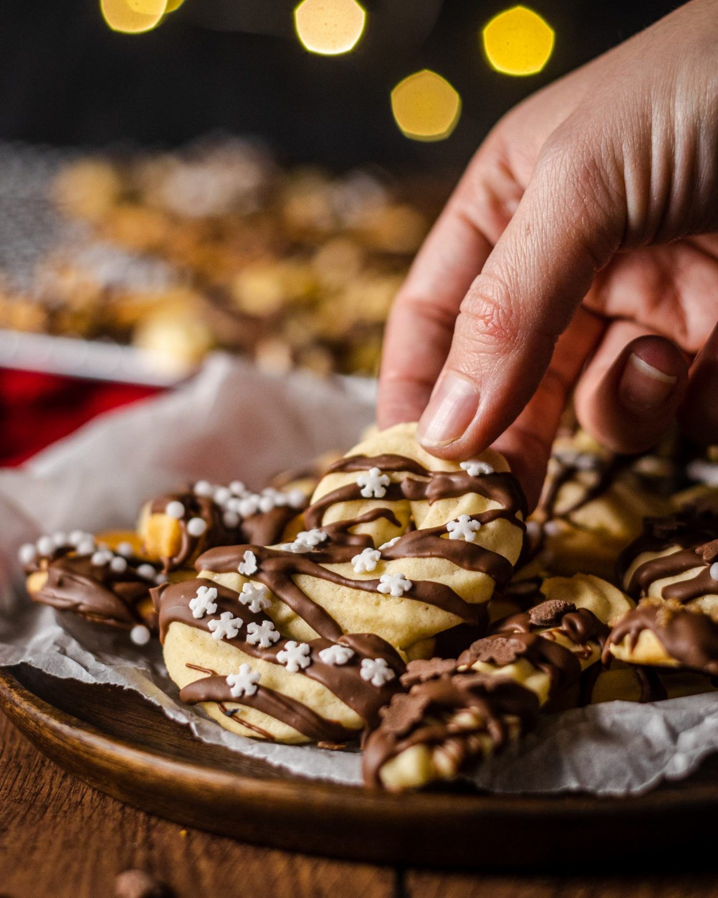 a hand picking up a vegan spritz cookie from a plate filled with cookies