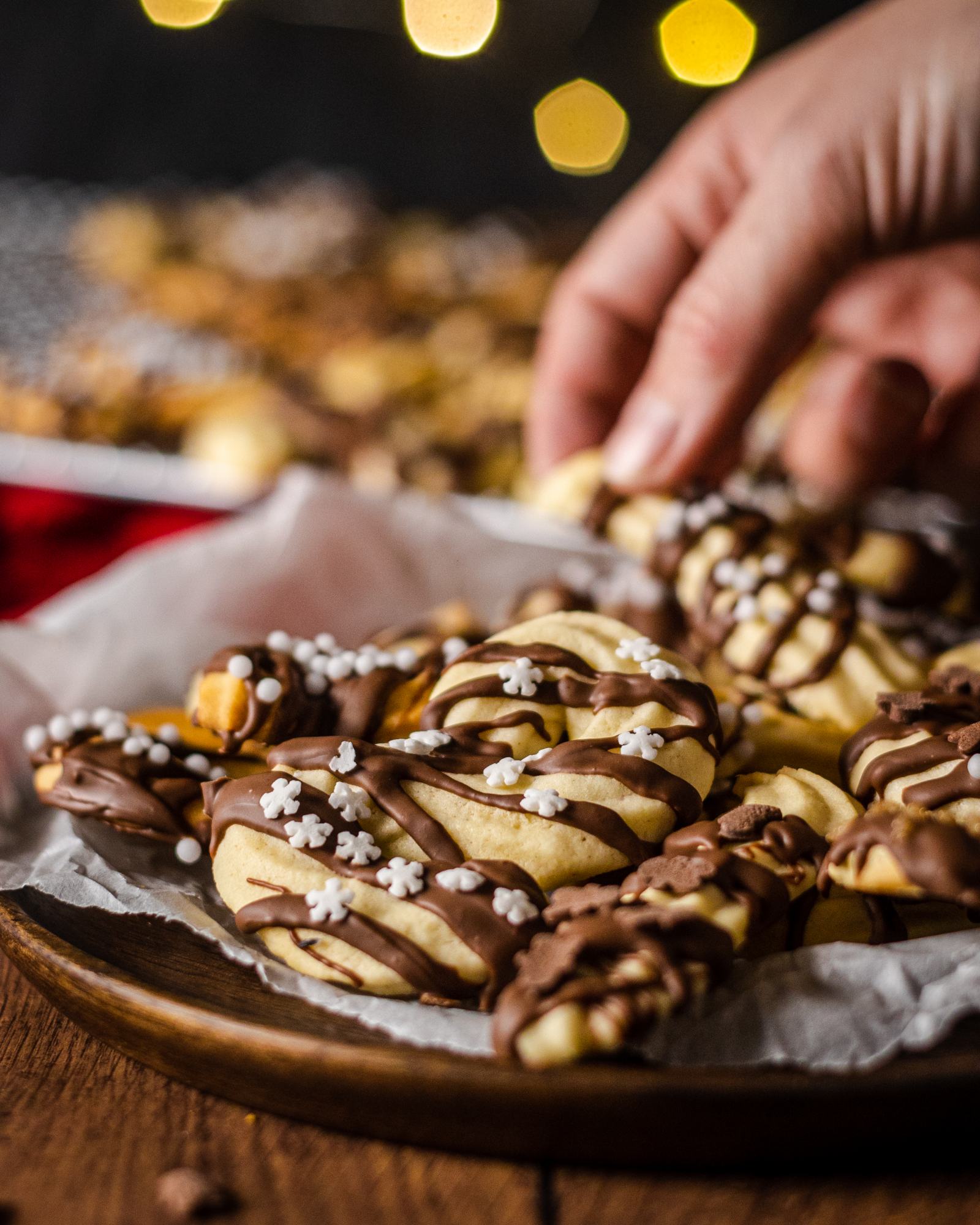 close up of a beautiful spritz cookie, a hand picking up a cookie in the background