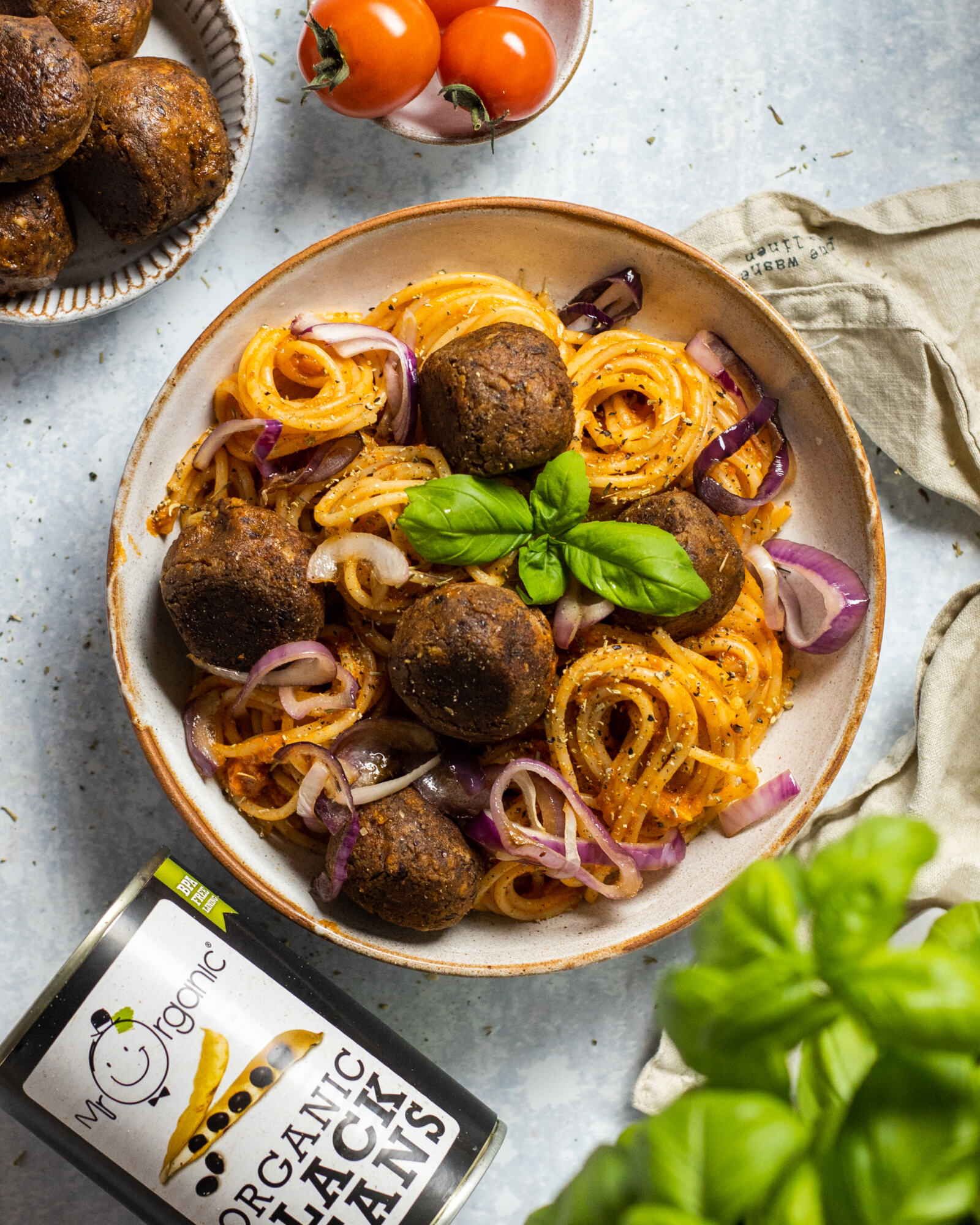 vegan black bean meatballs with spaghetti in a bowl with a tin of black beans next to the bowl