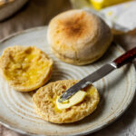 Sourdough English Muffin Recipe Vegan Sourdough Discard Recipe, 2 sourdough english muffins on a plate, one cut open and topped with vegan butter, super soft and fluffy