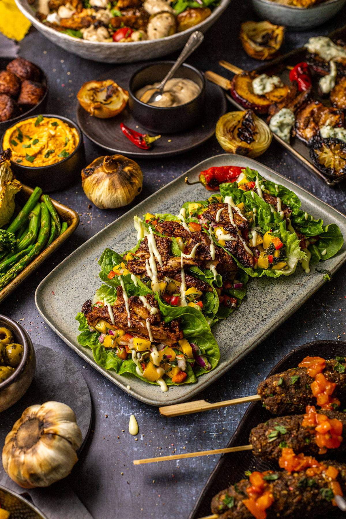 vegan BBQ food on a dark table with the lettuce tacos in the middle