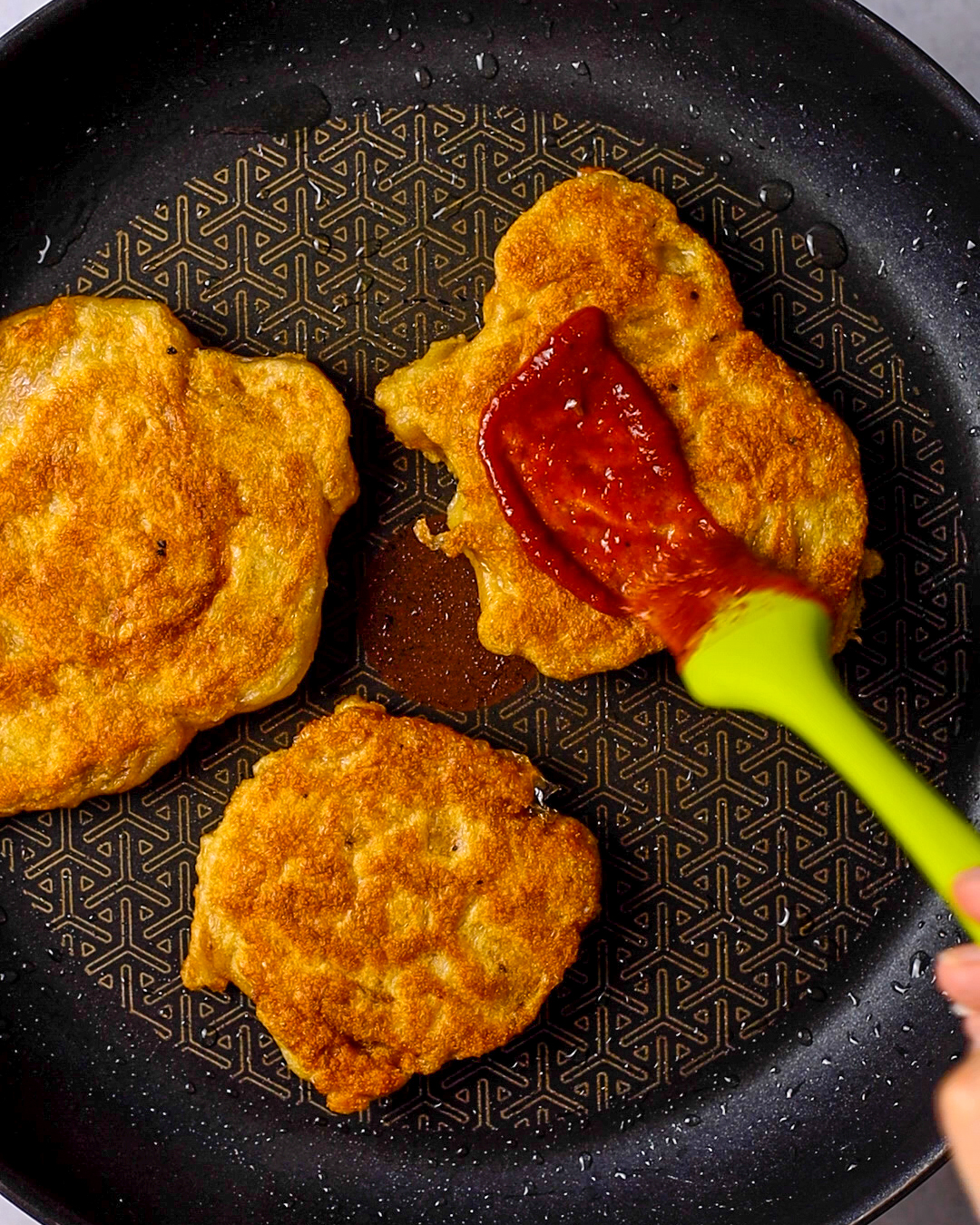 three vegan seitan chicken slices in a pan, being coated with bbq sauce