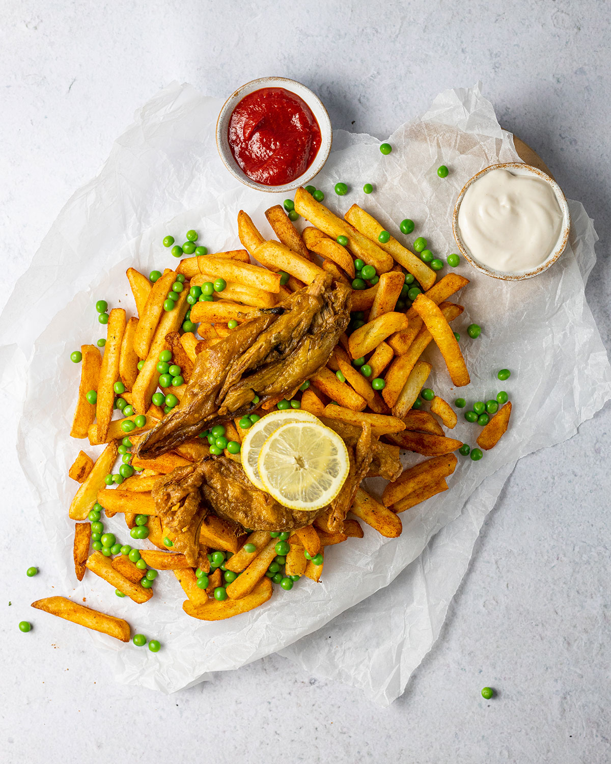 vegan fish and chips on white parchment paper with tomato ketchup and vegan mayo on the side