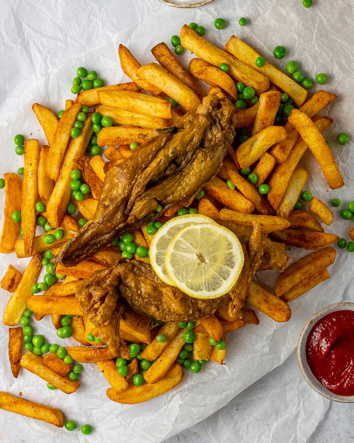 vegan banana blossom fish on a bed of thick-cut chips with herbs sprinkled on top and lemon slices placed on the side