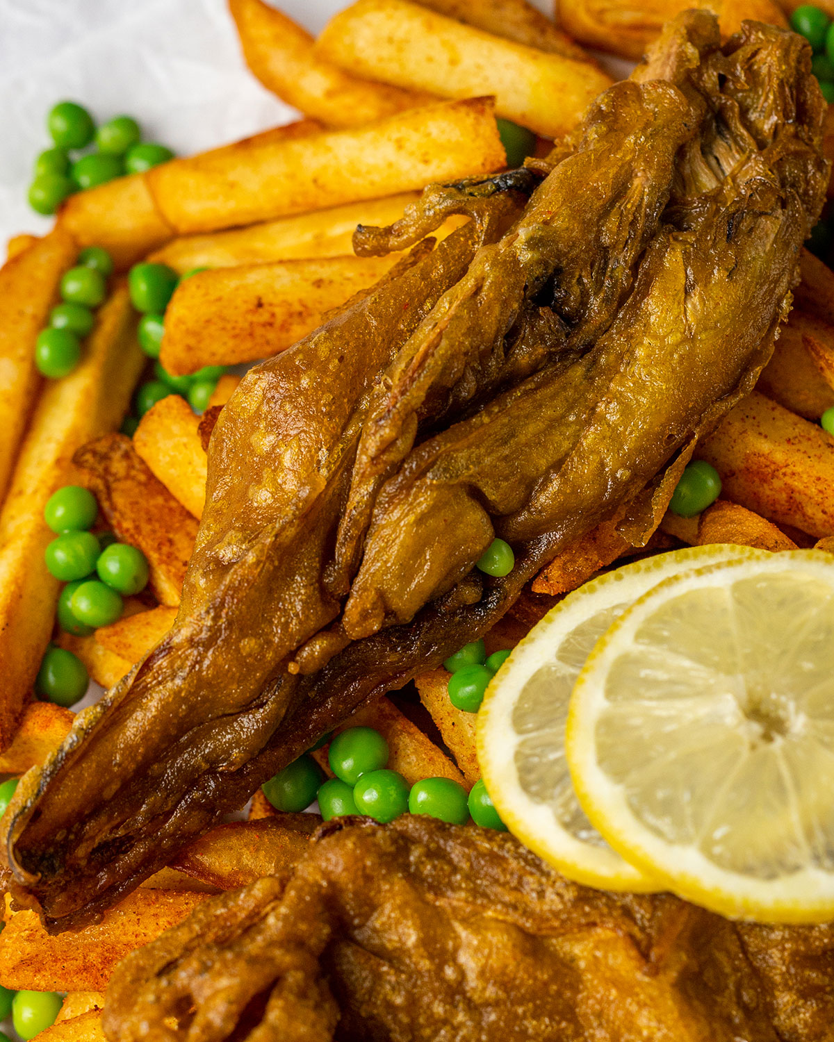 close up of crunchy vegan fish in beer batter on a bed of vegan chips with lemon slices next to it