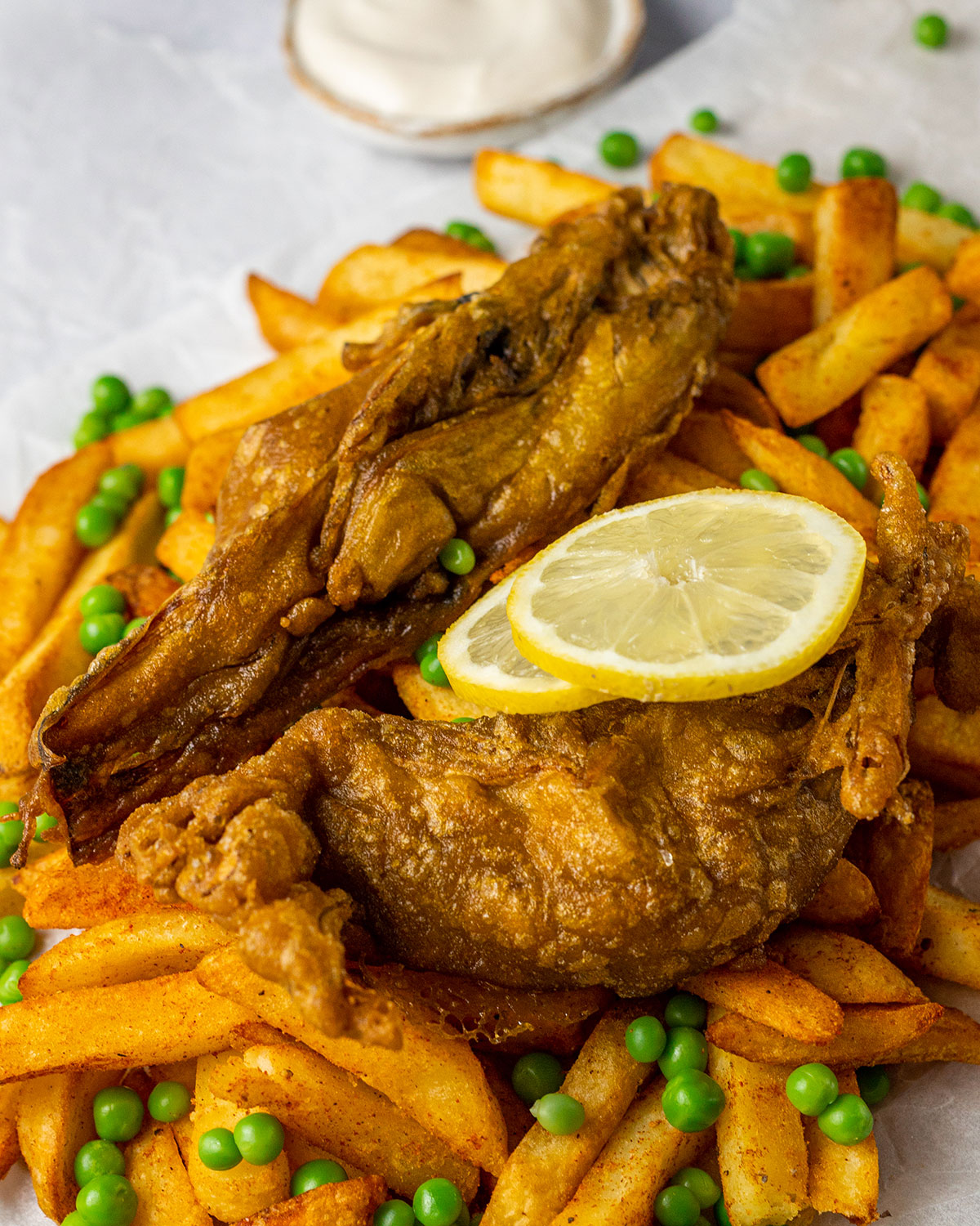 crispy vegan fish and chips next to vegan tartar sauce with peas and lemon slices