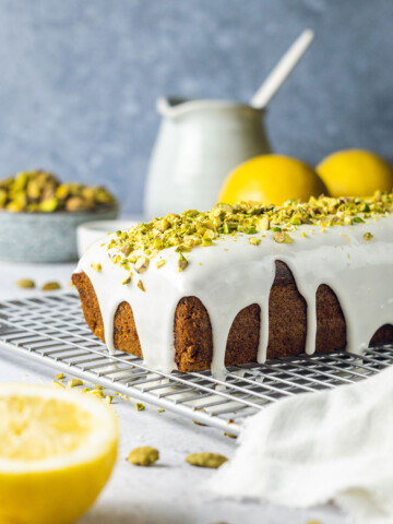 Vegan pistachio cake on a drying rack topped with lemon glaze and crushed pistachio nuts