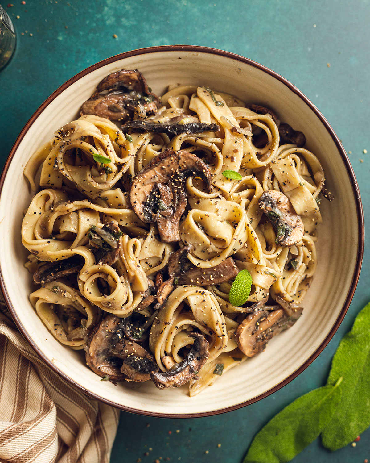 Creamy vegan mushroom pasta in a white bowl top with freshly cracked black pepper on a green backdrop