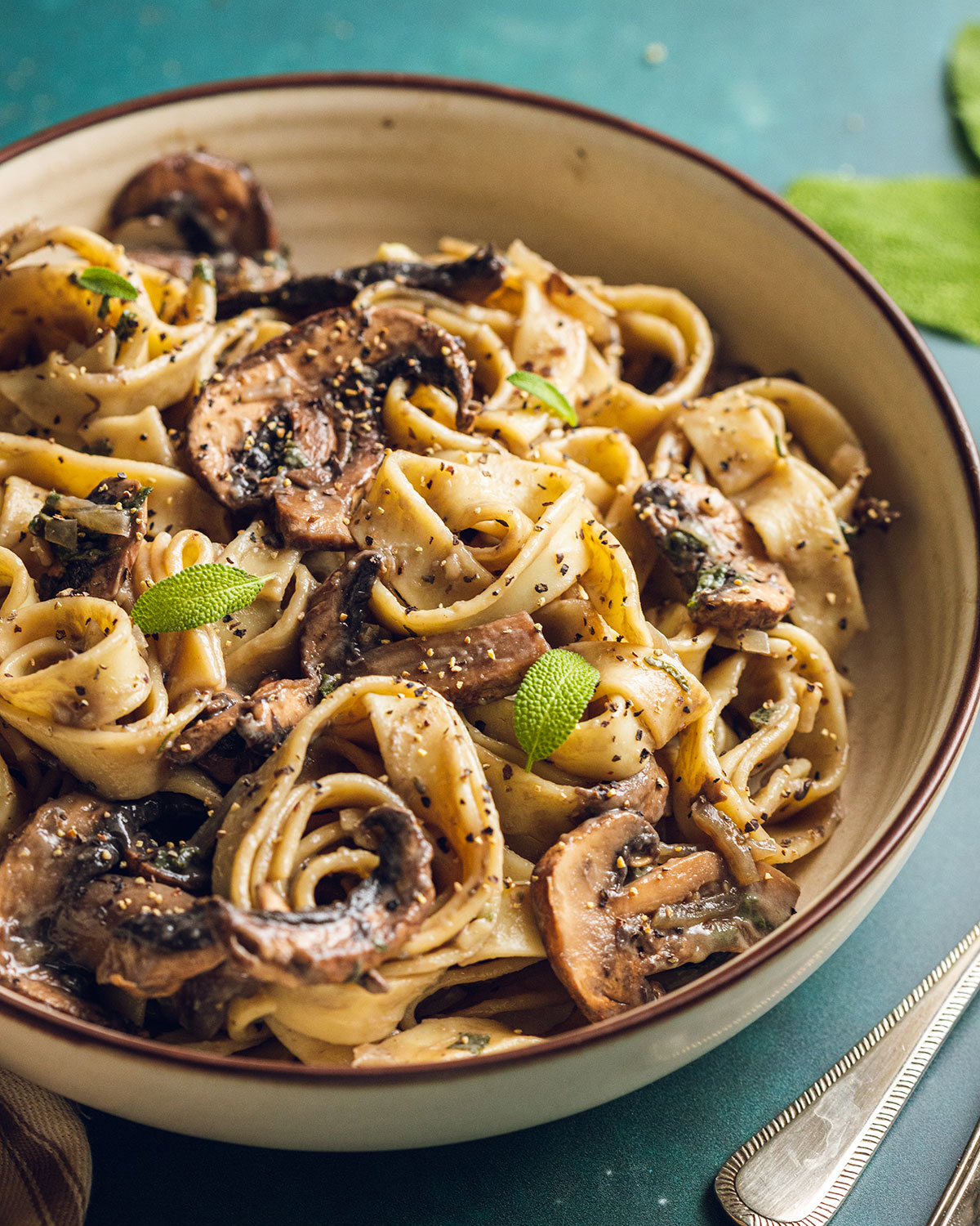 Creamy vegan mushroom pasta in a white bowl top with freshly cracked black pepper on a green backdrop