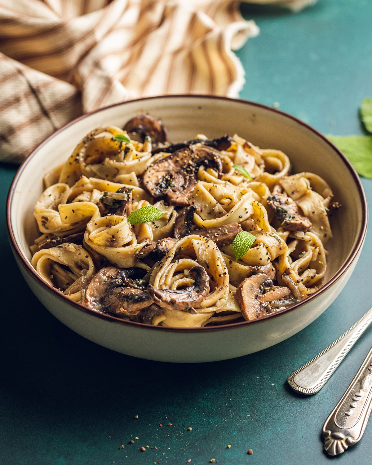 Creamy vegan mushroom pasta in a white bowl top with freshly cracked black pepper on a green backdrop