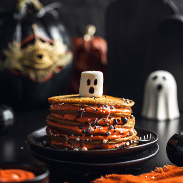 A stack of vegan pumpkin pancakes on a black plate with a ghost shaped marshmallow on top