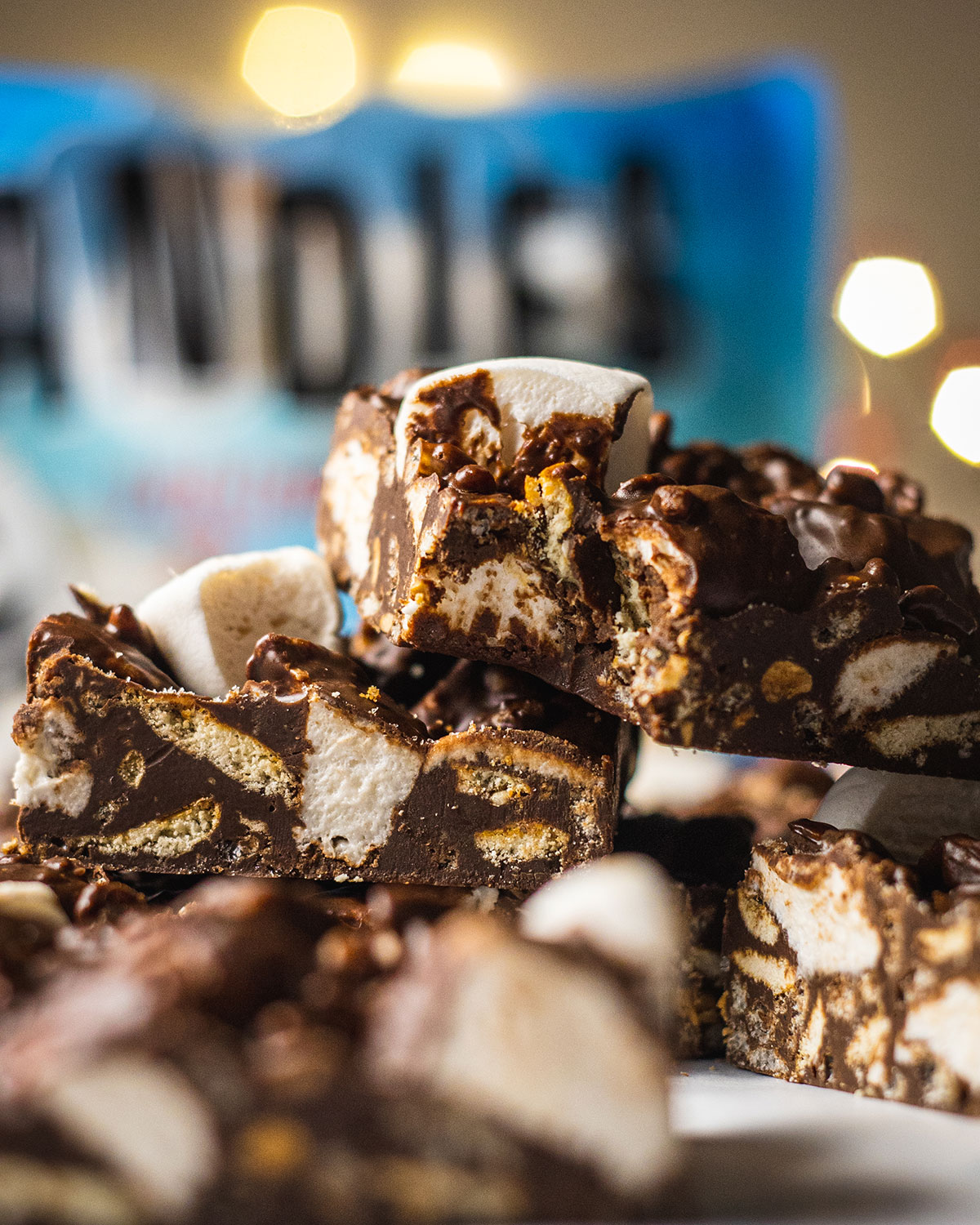 vegan rocky road slices on top of each other, shown up close, with a bite taken out of one of them and a blurry pack of vegan marshmallows in the background