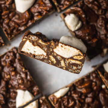 a slice of vegan rocky road with dark chocolate flipped up on a sheet full of vegan rocky road slices