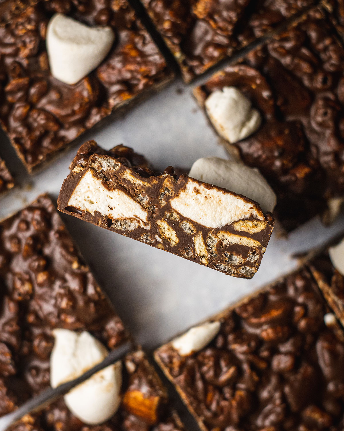 slices of vegan chocolate rocky road with a slice in the middle flipped up showing all the crunchy and vegan marshmallow layers