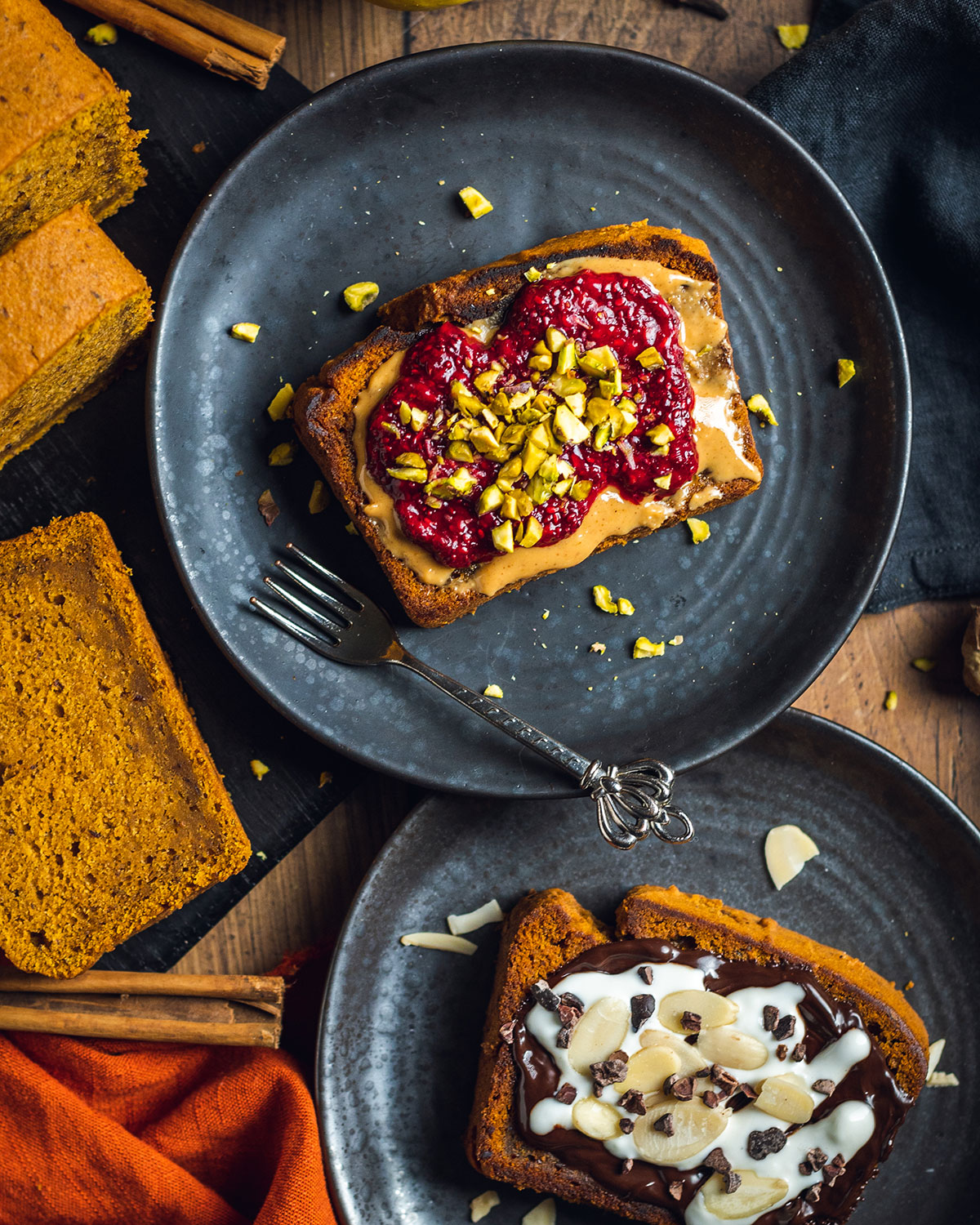 Two slices of vegan pumpkin loaf topped with different ingredients on two black plates, ready to serve.