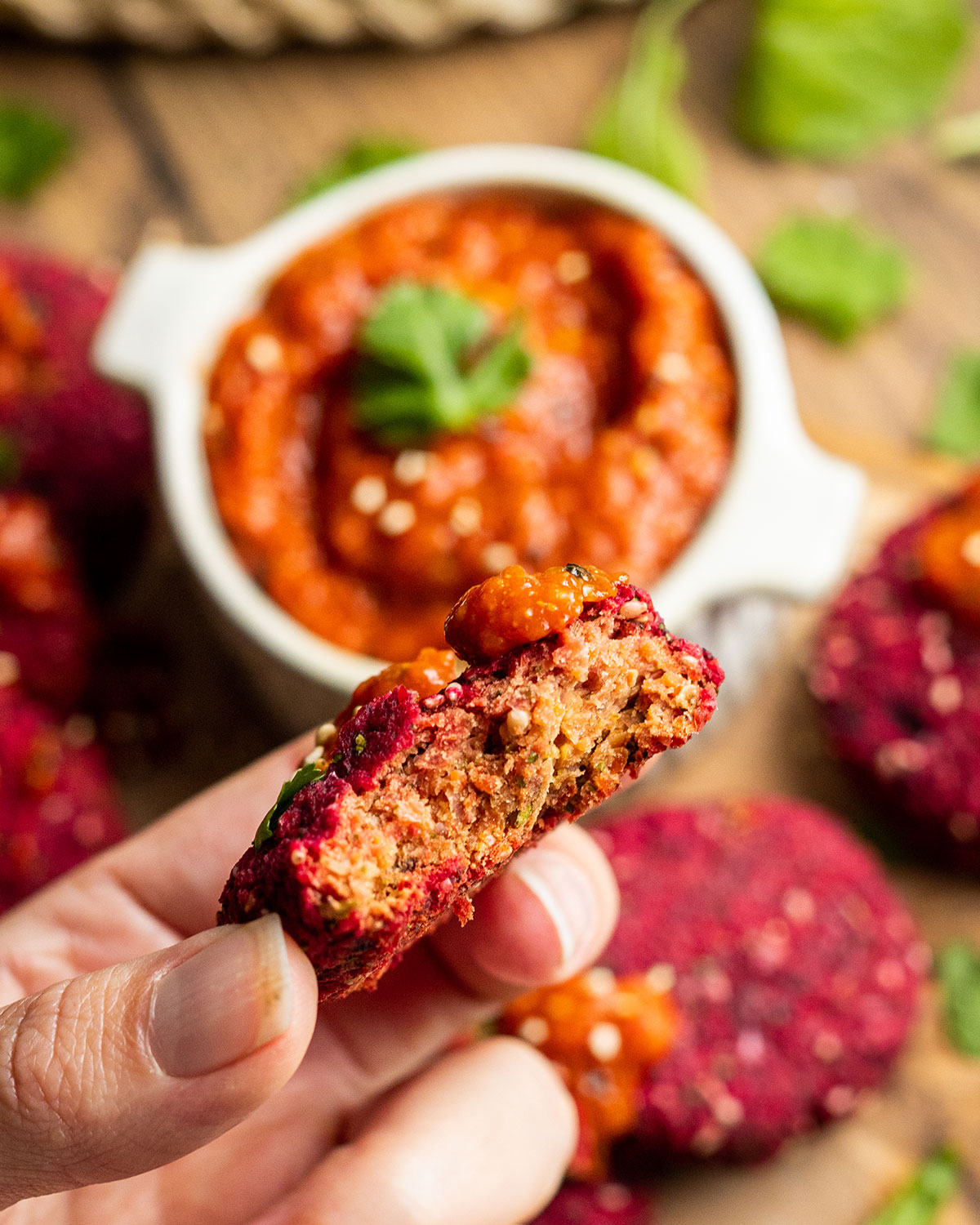 a hand holding a beetroot falafel with a bite taken out of it into the camera