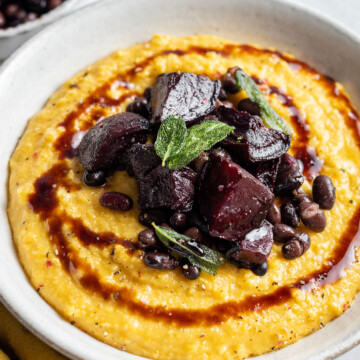 A full bowl of creamy pumpkin polenta topped with roasted beetroot black beans and a balsamic drizzle as well as crispy sage leaves.