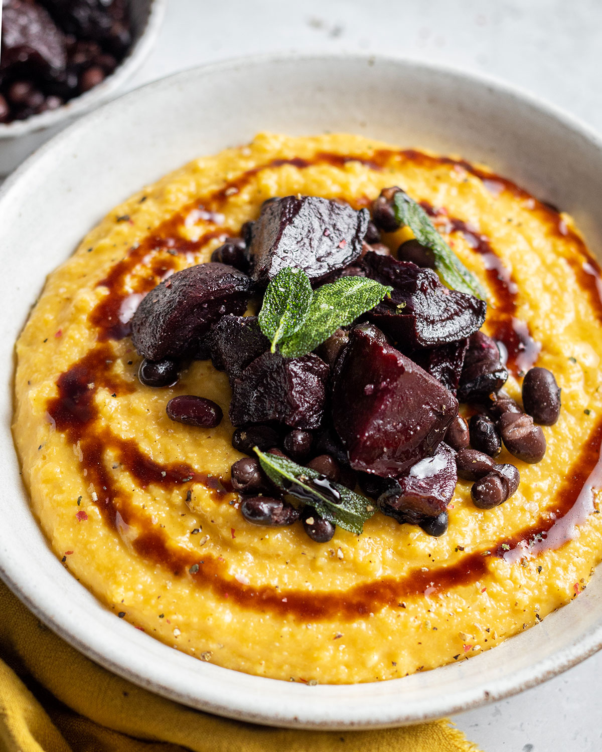 A full bowl of creamy pumpkin polenta topped with roasted beetroot black beans and a balsamic drizzle as well as crispy sage leaves.