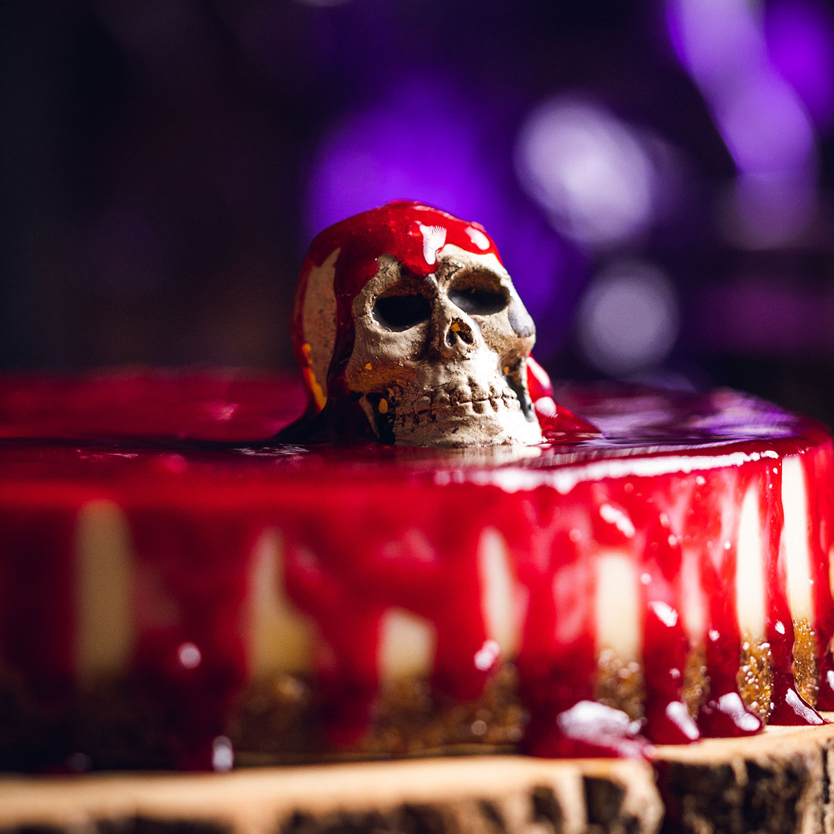 a vegan cheesecake decorated for halloween with a small skull on top and covered in raspberry coulis, a slice is cut out of the cake and visible in the background