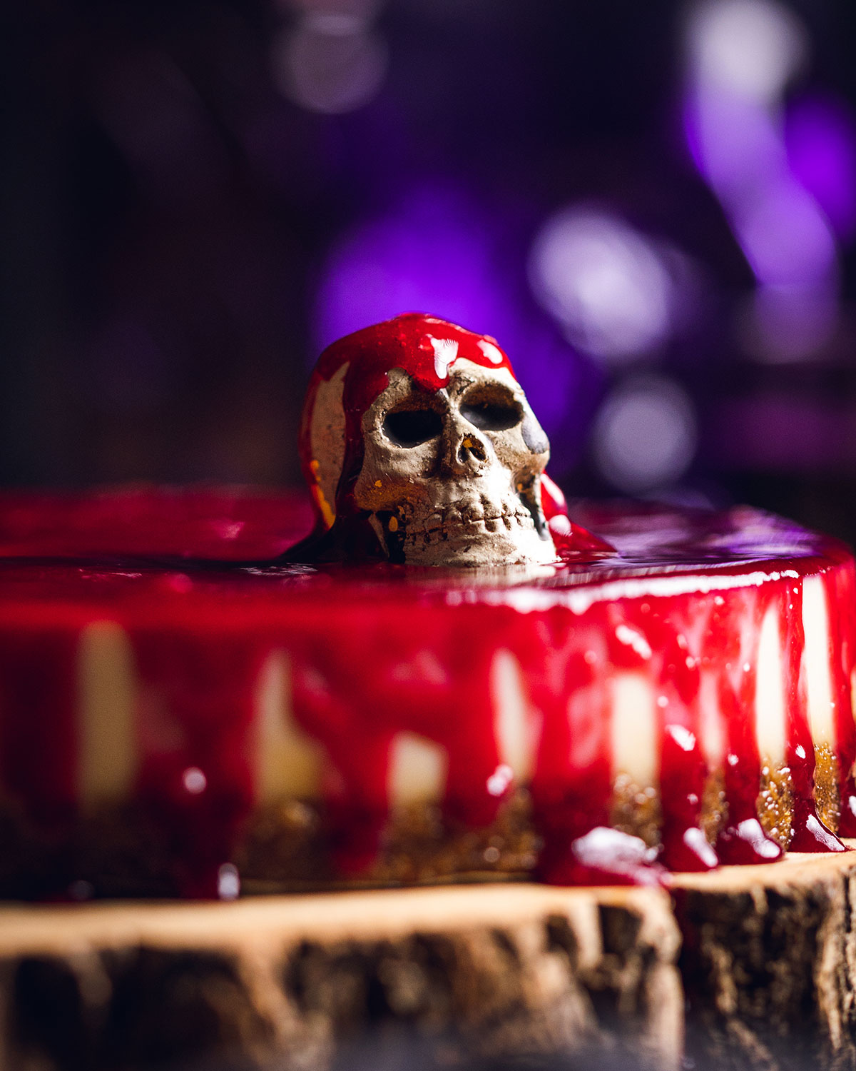 a small skull sitting on top of a halloween cheesecake with a glaze resembling blood over the top