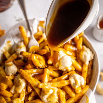 vegan poutine in a serving dish being drizzle with maple gravy