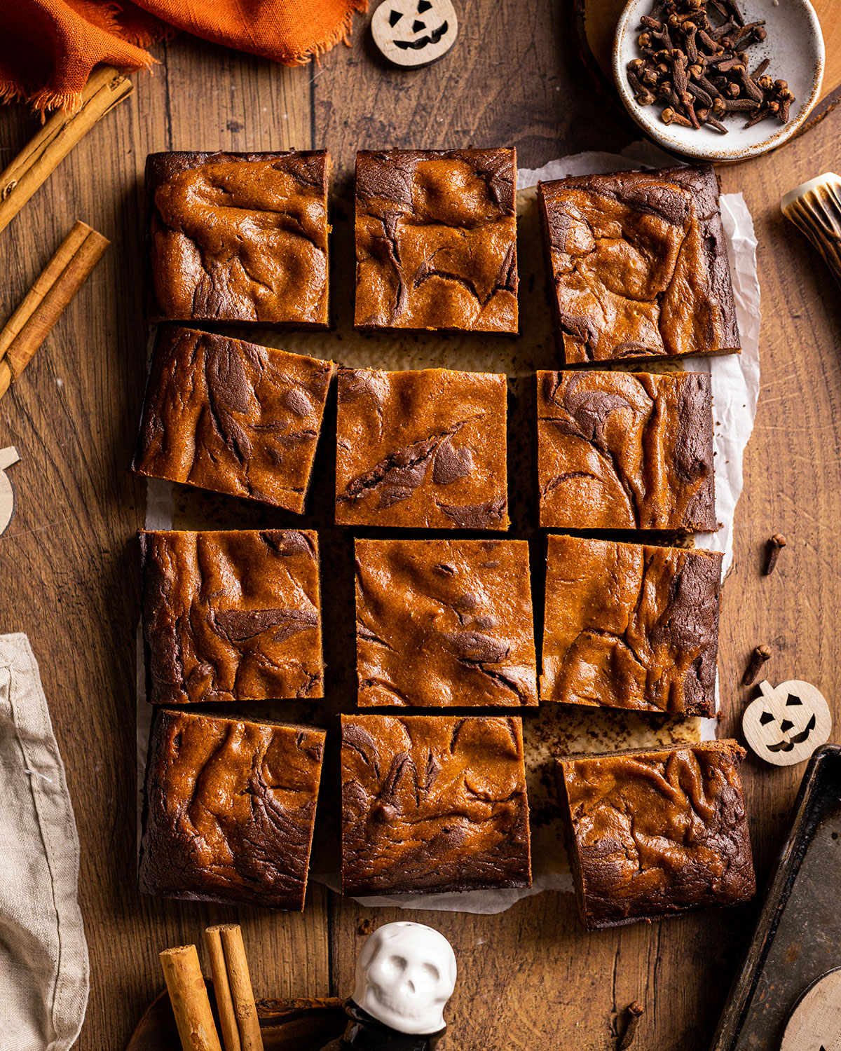 A sheet of baked pumpkin brownies cut into individual slices is sitting on a wooden table. 