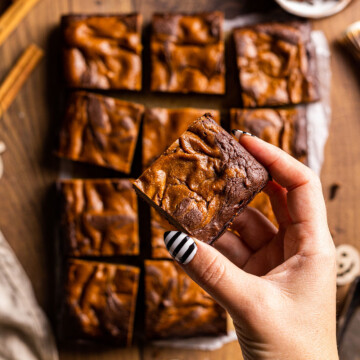 A hand holding a vegan pumpkin brownie above an entire sheet of the same baked brownies.