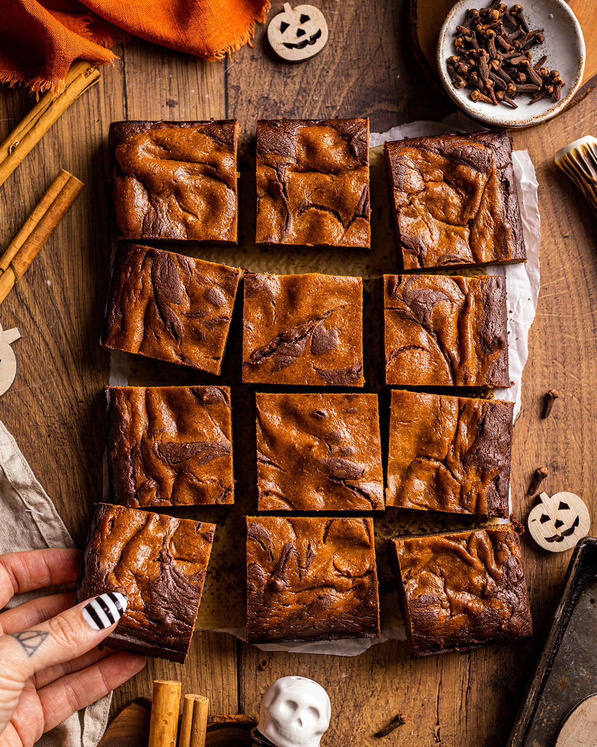 12 pumpkin brownies on a parchment, a hand picking up one