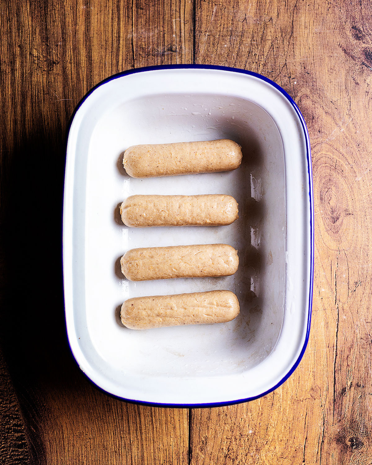 uncooked vegan sausages in an oven dish, arranged parallel