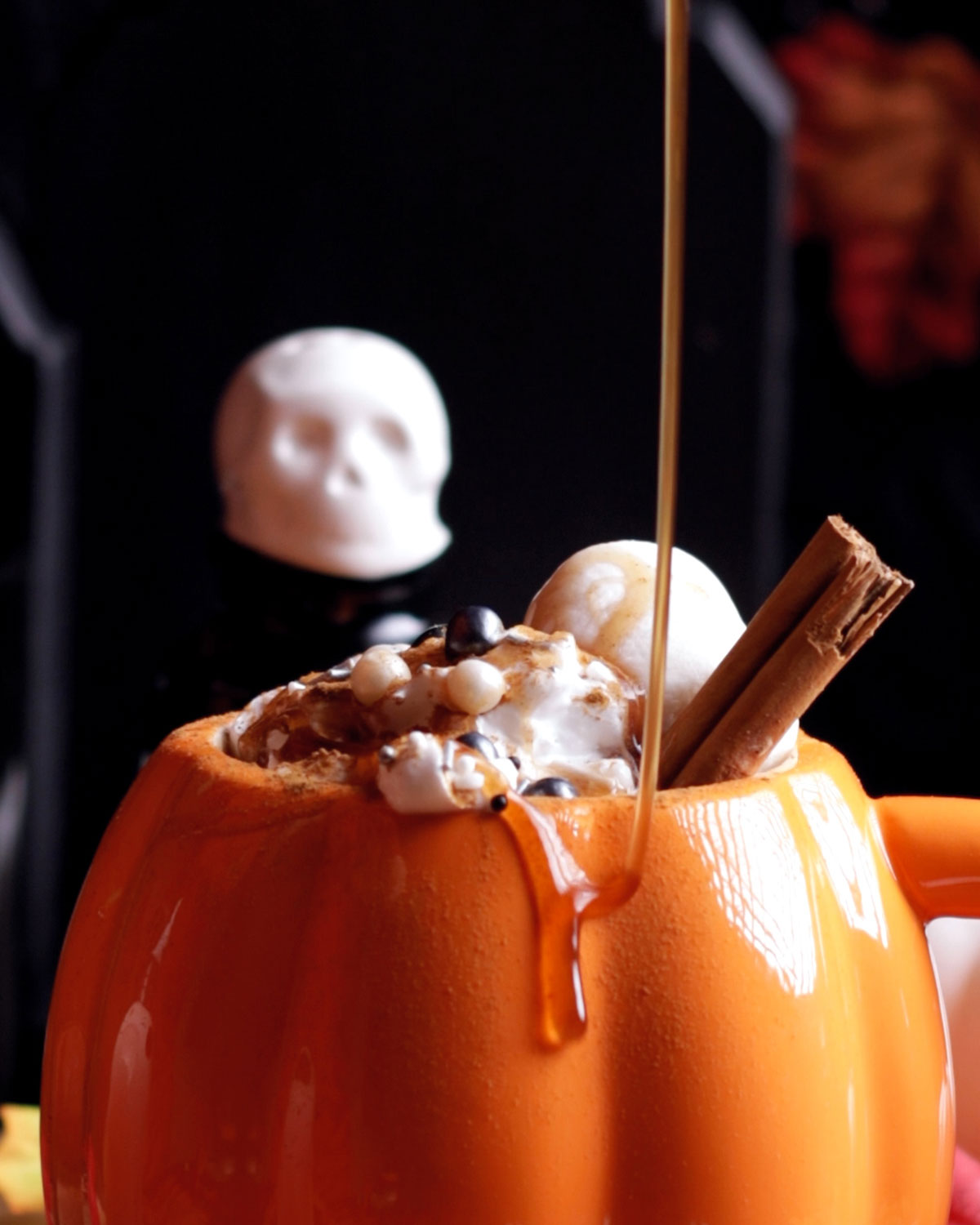 pumpkin spice syrup being drizzled onto a pumpkin spice latte in a pumpkin shaped mug