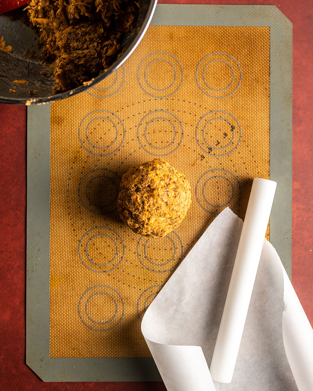 a ball of cracker dough in the middle of a silicone baking mat with a parchment paper and rolling pin next to it, about to be rolled out.