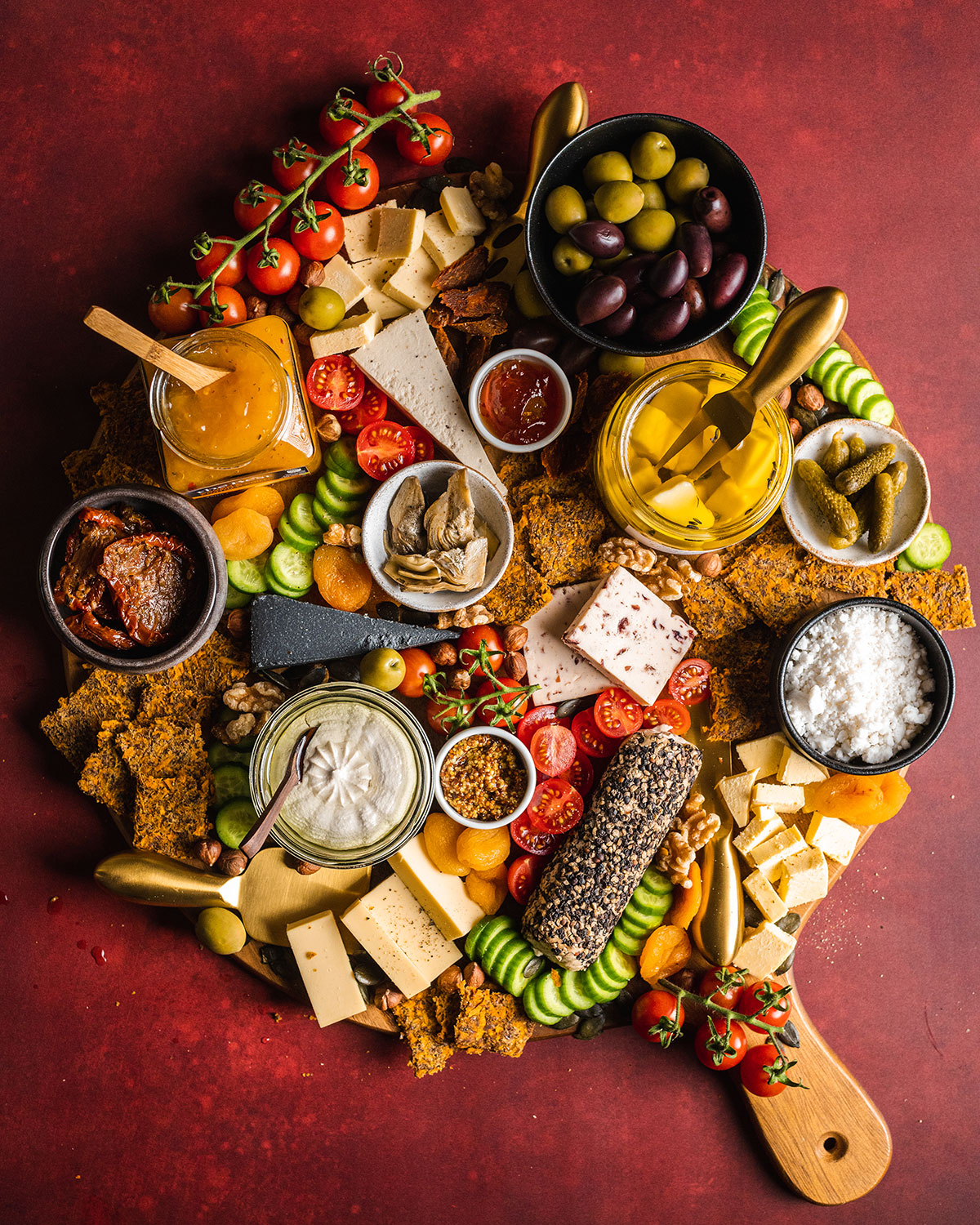 A large round cheeseboard fully packed with a selection of nut cheeses, chutneys, fruit, veg and homemade sweet potato crackers