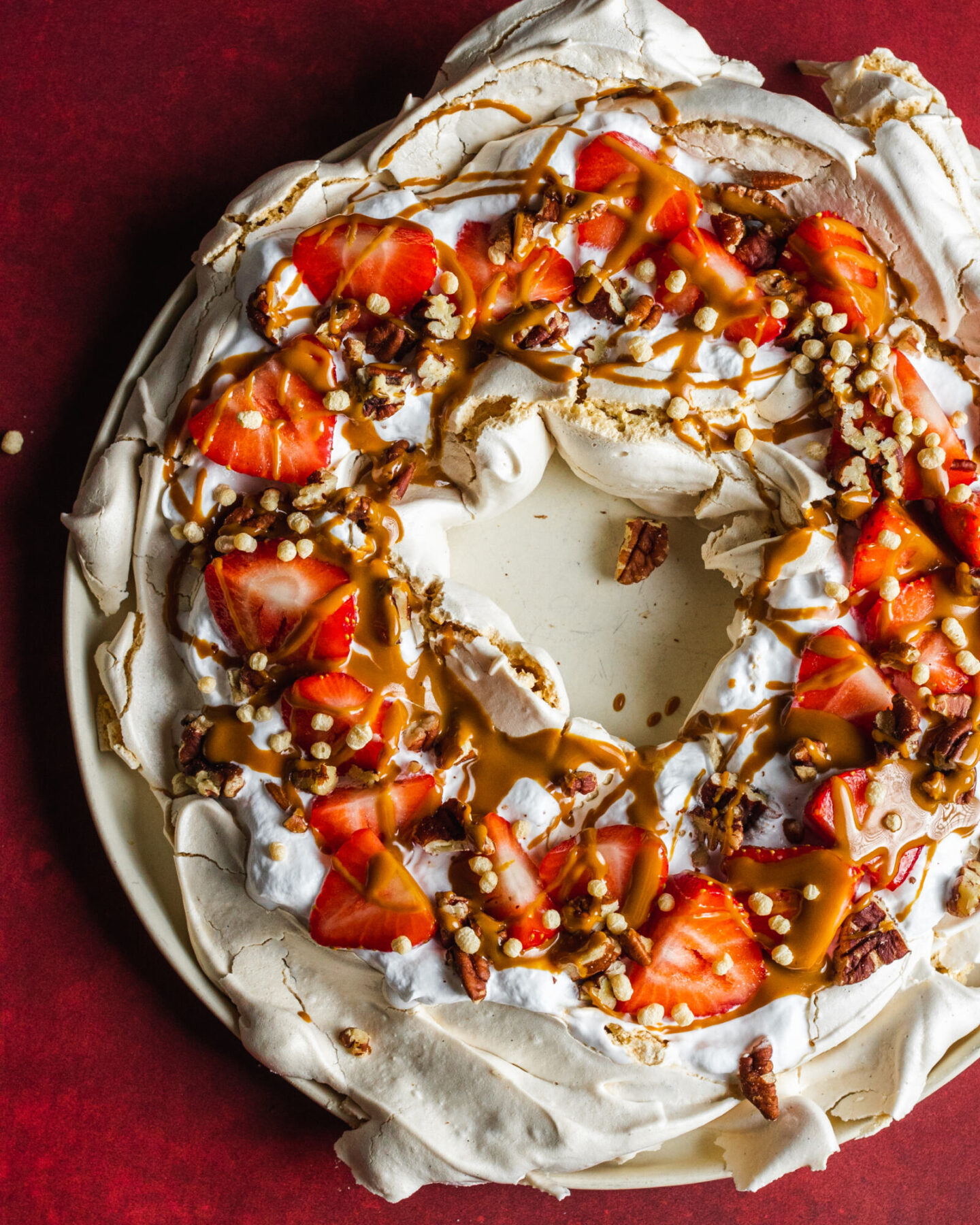 Vegan pavlova wreath made with aqauafaba meringue, topped with strawberries, whipped coconut cream and toasted pecan nuts