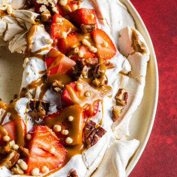 Vegan pavlova wreath made with aqauafaba meringue, topped with strawberries, whipped coconut cream and toasted pecan nuts